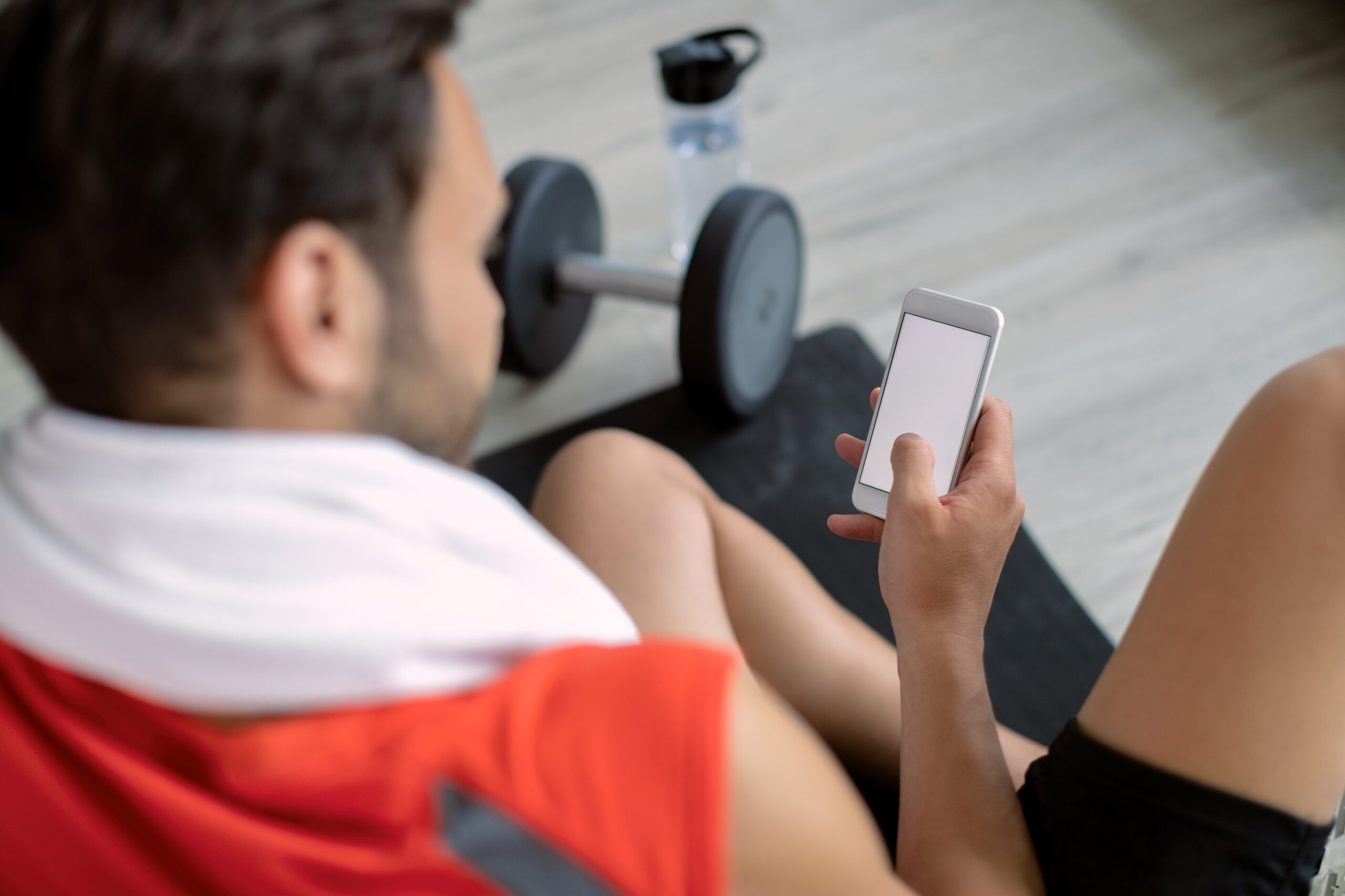 Close-up of athletic man texting on smart phone in health club. Copy space.